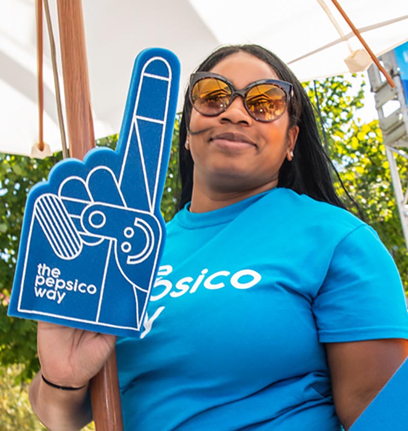 Woman smiling with a foam finger with "The PepsiCo Way" logo on it