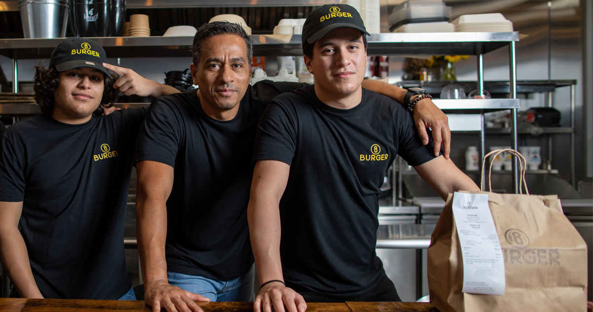 Jesus Daza standing in between his sons in the kitchen of their restaurant, 8 Burger.