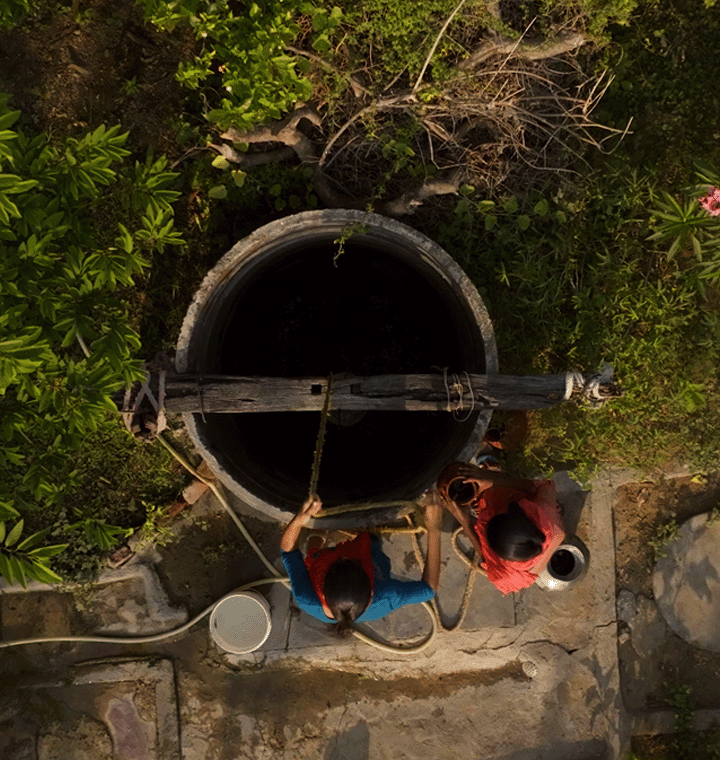 Women pull up water in a bucket from a well